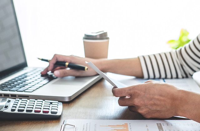 Bookkeeper reviewing financial records on a laptop with a calculator