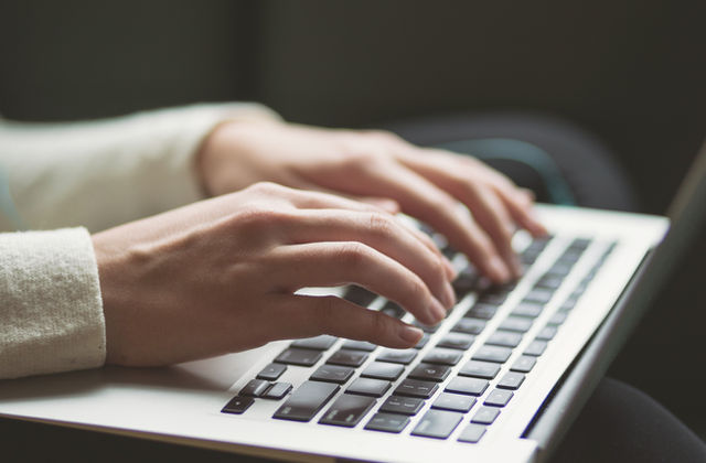 Hands typing on a laptop while preparing grant documents